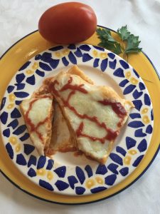 Lasaña boloñesa recién salida del horno presentada en un plato en el que aparece un tomate entero y una rama de perejil.