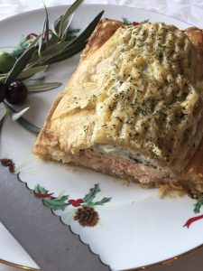 Presentación de hojaldre de salmón con crema de espinacas en un plato con motivos navideños