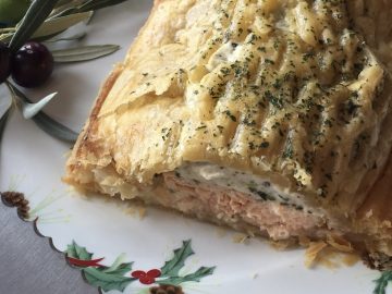 Presentación de hojaldre de salmón con crema de espinacas en un plato con motivos navideños