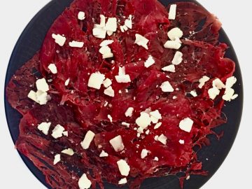 Carpaccio de vacuno con queso parmigiano sobre un plato negro