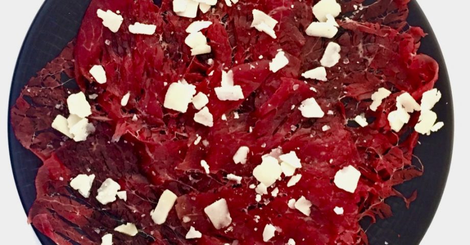 Carpaccio de vacuno con queso parmigiano sobre un plato negro