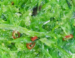 Detalle de ensalada de algas wakame en el que se puede apreciar el verde intenso y luminoso así como las semillas de sésamo y el rojo brillante del chile en rodajas.