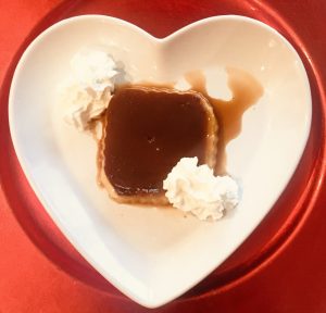 Tocinillo de cielo de forma cuadrada sobre un plato en forma de corazón blanco y un sobre plato rojo