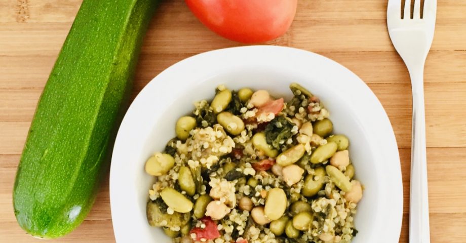 Quinoa con verduritas salteadas. Sobre una tabla color madera aparece un bol con el salteado. Alrededor hay un calabacín, un tomate y un tenedor.