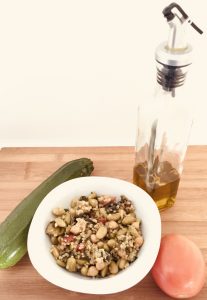 Presentación del plato con el salteado de quinoa y verduras junto a un calabacín, un tomate y una botella de aceite.