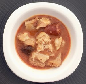 Plato de callos a la madrileña. Están en un bol blanco y un bajoplato negro. Se ven la morcilla el chorizo y los callos.