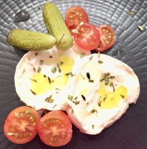 Tapa de mozzarella con cherry y pepinillos. Sobre un plato negro con aceite y orégano.Menú Día de la Madre.